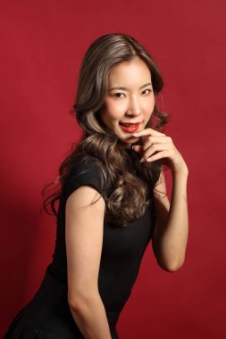 Kırmızı arka planda duran siyah elbiseli Asyalı kadın..