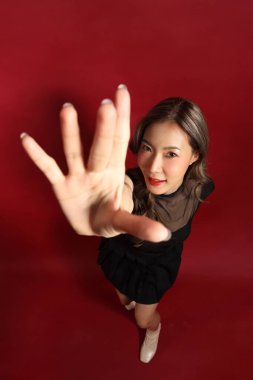 Kırmızı arka planda duran siyah elbiseli Asyalı kadın..