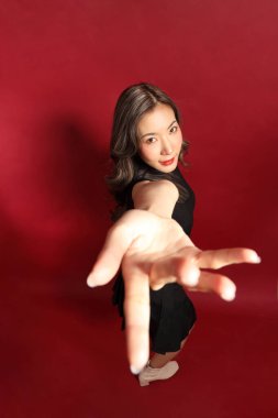 Kırmızı arka planda duran siyah elbiseli Asyalı kadın..