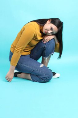 Yeşil arka planda oturan sıradan giysili Asyalı kadın..