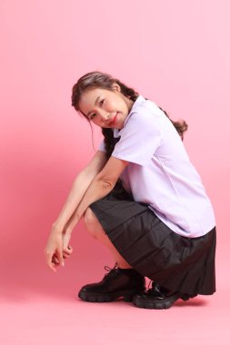 Pembe arka planda oturan Taylandlı öğrenci üniformalı Asyalı kız..