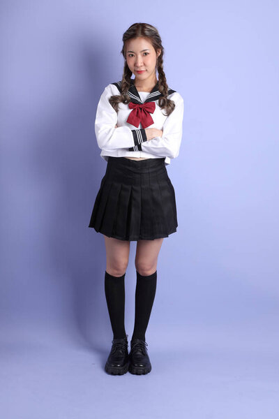 The Asian girl in Japanese student uniform standing on the purple background.