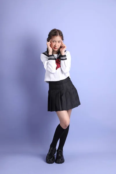 The Asian girl in Japanese student uniform standing on the purple background.
