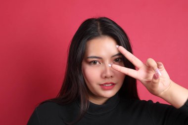 Kırmızı arka planda duran siyah elbiseli Asyalı kadın..