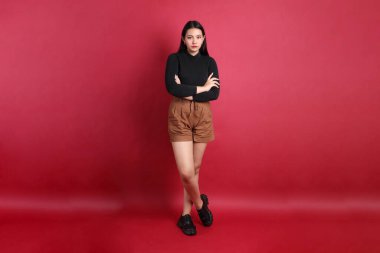 Kırmızı arka planda duran siyah elbiseli Asyalı kadın..