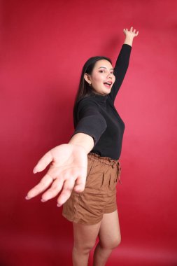 Kırmızı arka planda duran siyah elbiseli Asyalı kadın..