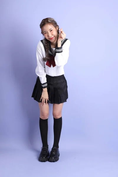 身穿日本校服的亚洲女孩站在紫色的背景上 — 图库照片