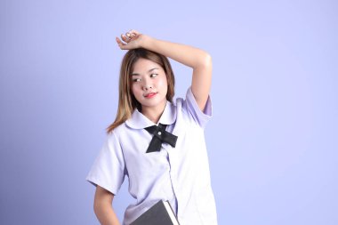 Mor arka planda duran Taylandlı öğrenci üniformalı Asyalı kız..