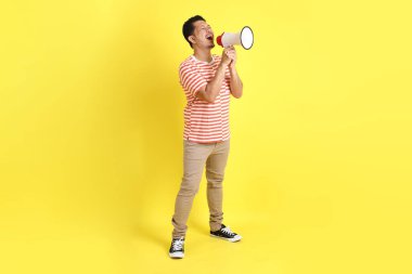 Sarı arka planda dikilen sıradan giysili yetişkin Asyalı adam..