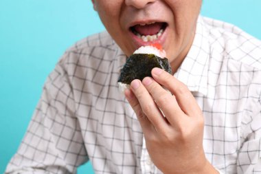 Yeşil arka planda onigiri yiyen Asyalı adam..