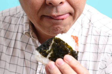 Yeşil arka planda onigiri yiyen Asyalı adam..