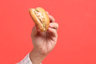 Turuncu arka planda hamburgeri tutan Asyalı adam..