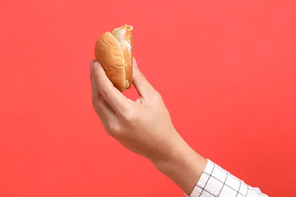 オレンジ色の背景にハンバーガーを握っているアジアの男 — ストック写真