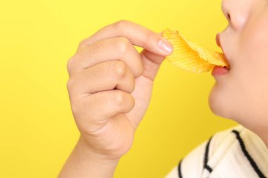 Sarı arka plandaki elden patates cipsi yiyen Asyalı kadın..