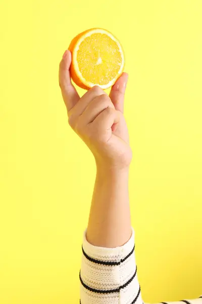 The Asian woman holding orange in the hand on the yellow background.
