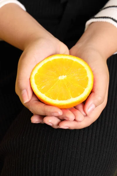 The Asian woman holding orange in the hand on the yellow background.