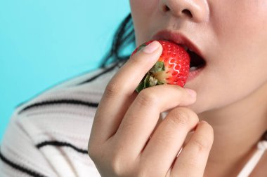 Asyalı kadın yeşil arka planda elinden çilek yiyor..