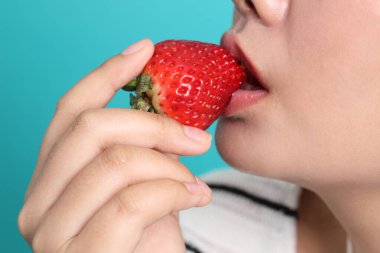 Asyalı kadın yeşil arka planda elinden çilek yiyor..