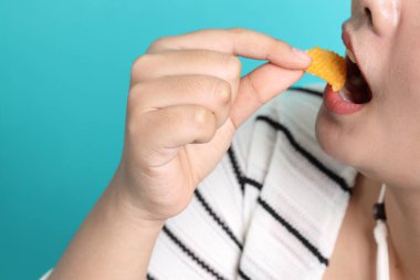 Sarı arka plandaki elden patates cipsi yiyen Asyalı kadın..