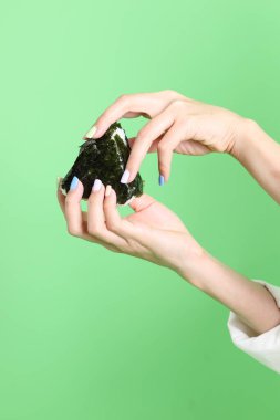 Onigiri 'yi tutan Asyalı kadın yeşil arka planda Japon yemeği..