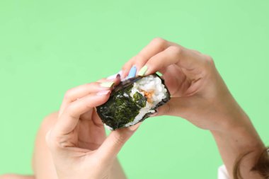 Onigiri 'yi tutan Asyalı kadın yeşil arka planda Japon yemeği..