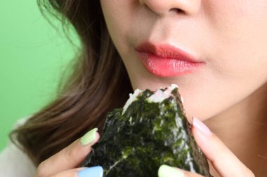 Asyalı kadın yeşil arka planda elinde Japon yemeği ile onigiri yiyor..