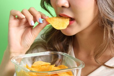 Yeşil arka plandaki elden patates cipsi yiyen Asyalı kadın..