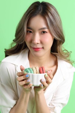 Sarı arka planda elinde badem kurabiyesi tutan Asyalı kadın..