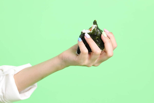 Азиатка держит онигири японскую еду в руке на зеленом фоне.