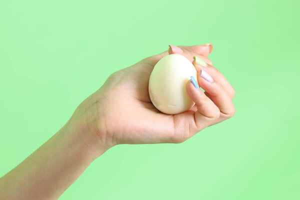 Азиатка держит яйцо в руке на зеленом фоне.