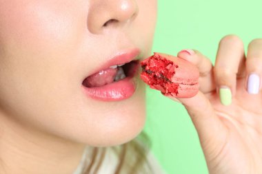 Sarı arka planda elden badem kurabiyesi yiyen Asyalı kadın..