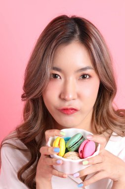 Pembe arka planda elinde kurabiye tutan Asyalı kadın..