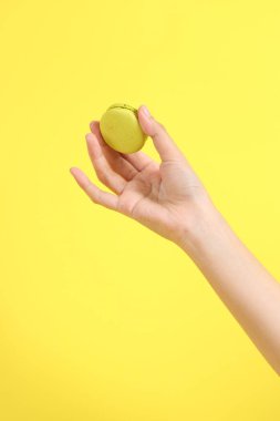 Sarı arka planda elden badem kurabiyesi yiyen Asyalı kadın..