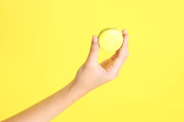 Sarı arka planda elden badem kurabiyesi yiyen Asyalı kadın..