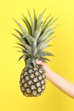 Sarı arka planda ananas tutan Asyalı kadın..