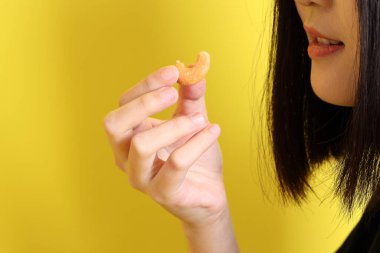 Sarı arka planda fındık tutan Asyalı kadın..