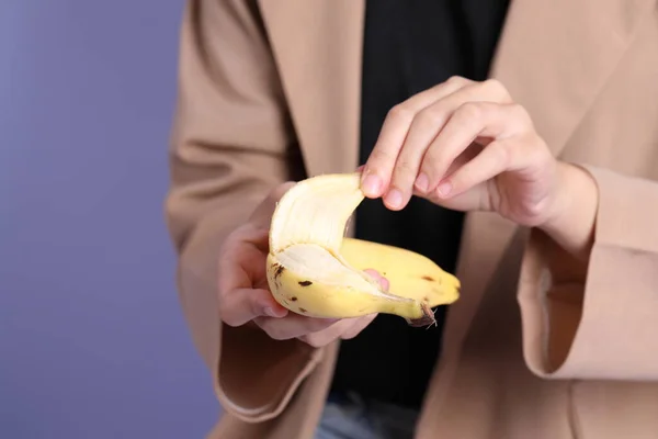 The Asian woman eating banana from the hand on the purple background.