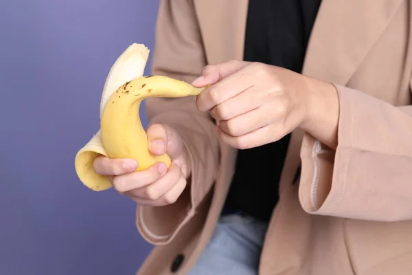 The Asian woman eating banana from the hand on the purple background.