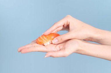 Mavi arka planda sushi tutan Asyalı kadın..