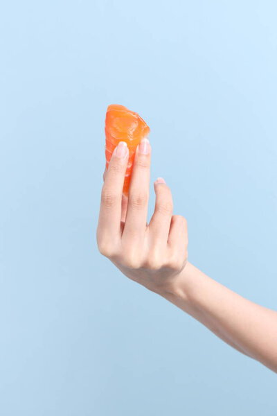 The Asian woman hand holding sushi in the blue background.