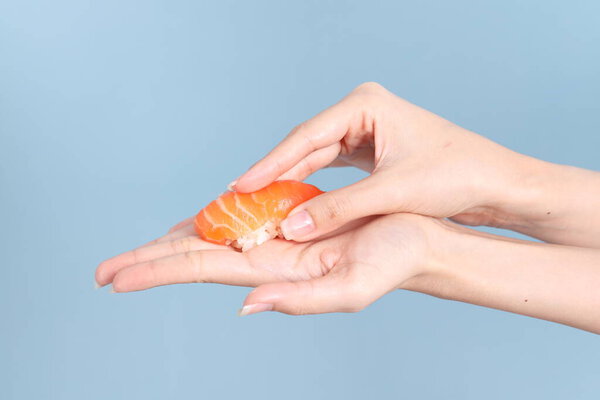 The Asian woman hand holding sushi in the blue background.