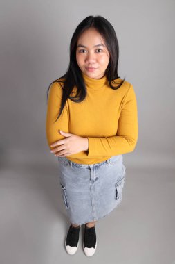 Güneydoğu Asyalı kadının üstten görünüşü. Gri arka planda tam boy giyinmiş, günlük sarı giyinmiş..