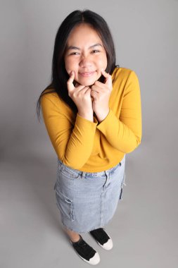 Güneydoğu Asyalı kadının üstten görünüşü. Gri arka planda tam boy giyinmiş, günlük sarı giyinmiş..