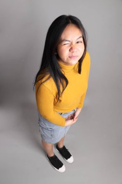 Güneydoğu Asyalı kadının üstten görünüşü. Gri arka planda tam boy giyinmiş, günlük sarı giyinmiş..