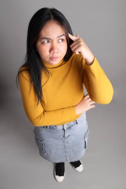 Güneydoğu Asyalı kadının üstten görünüşü. Gri arka planda tam boy giyinmiş, günlük sarı giyinmiş..