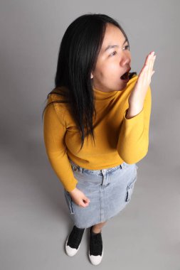 Güneydoğu Asyalı kadının üstten görünüşü. Gri arka planda tam boy giyinmiş, günlük sarı giyinmiş..