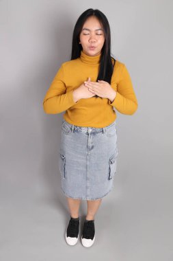 Güneydoğu Asyalı kadının üstten görünüşü. Gri arka planda tam boy giyinmiş, günlük sarı giyinmiş..