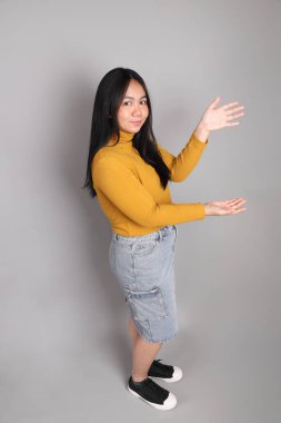 Güneydoğu Asyalı kadının üstten görünüşü. Gri arka planda tam boy giyinmiş, günlük sarı giyinmiş..