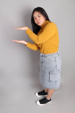 Güneydoğu Asyalı kadının üstten görünüşü. Gri arka planda tam boy giyinmiş, günlük sarı giyinmiş..