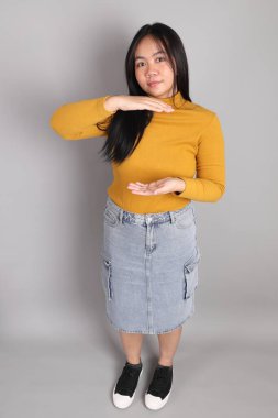 Güneydoğu Asyalı kadının üstten görünüşü. Gri arka planda tam boy giyinmiş, günlük sarı giyinmiş..